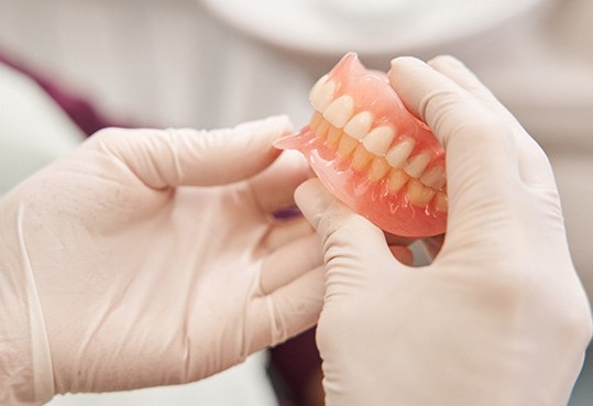 White-gloved hands holding complete set of dentures