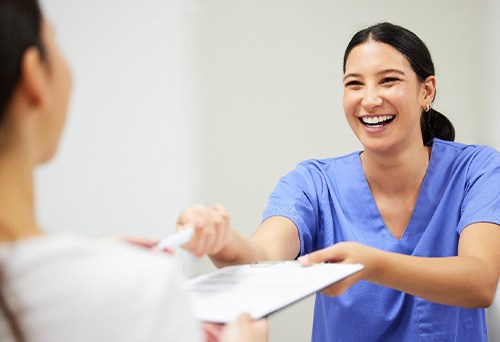 Dental staff smiling while helping patient with paperwork