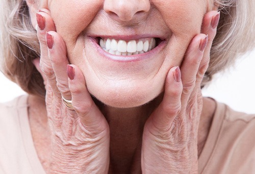 Nose-to-neck view of older woman smiling and holding hands to her cheeks