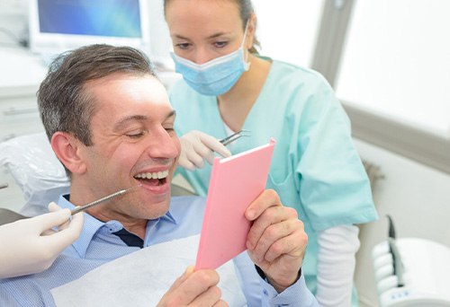 Man in dental chair smiling into mirror with dentist looking over his shoulder