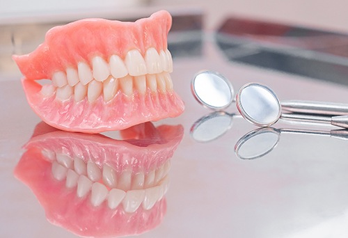 profile view of complete set of dentures with dental mirrors on reflective surface