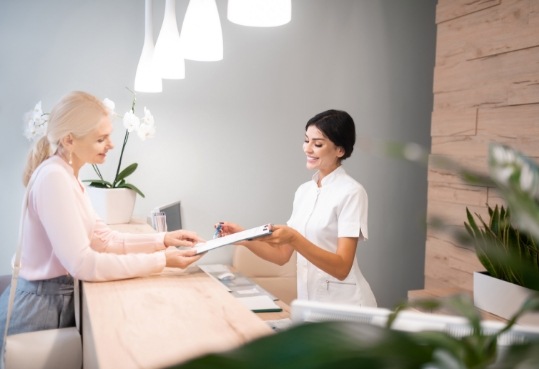 Dental receptionist handing a clipboard to a patient