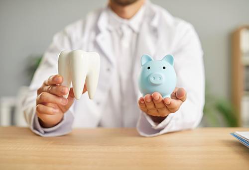 a dentist holding a model tooth and a piggy bank 