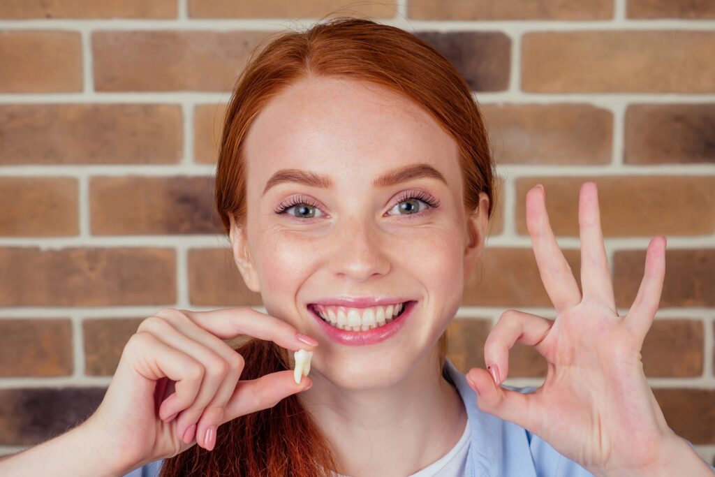 Woman holding extracted tooth in one hand and making "ok" sign with the other