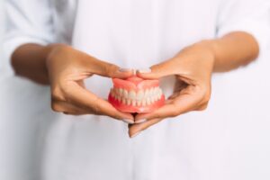 Dentist in white coat holding out dentures in front of them.